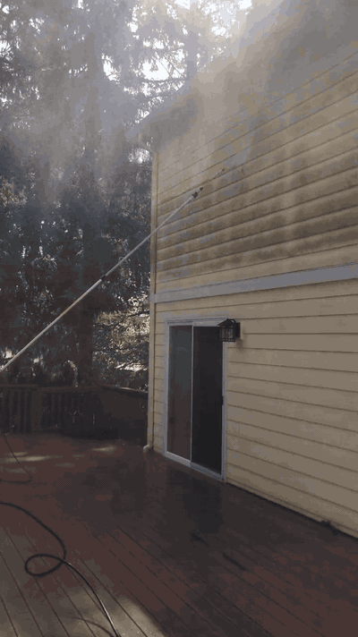 Portland-area home with yellow vinyl siding being soft-washed — dirty streaks above, clean siding below
