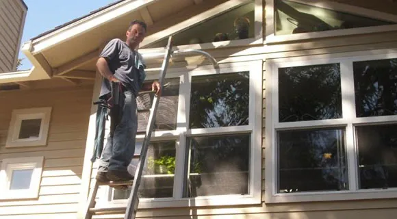 USA Gutter crew member squeegeeing a freshly washed window on a Portland home during a spring cleaning visit